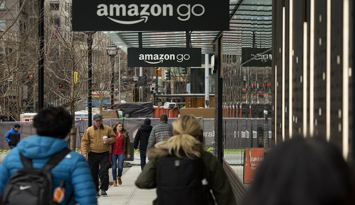 Pedestrians walk past the new Amazon.com Inc. Go grocery store in Seattle, Washington, U.S., on Wednesday, March 8, 2017. Amazon's goal is to become a Top 5 grocery retailer by 2025, according to a person familiar with the matter. That would require more than $30 billion in annual food and beverage spending through its sites, up from $8.7 billion including Amazon Fresh and all other food and drink sales in 2016, according to Cowen & Co. Photographer: David Ryder/Bloomberg via Getty Images